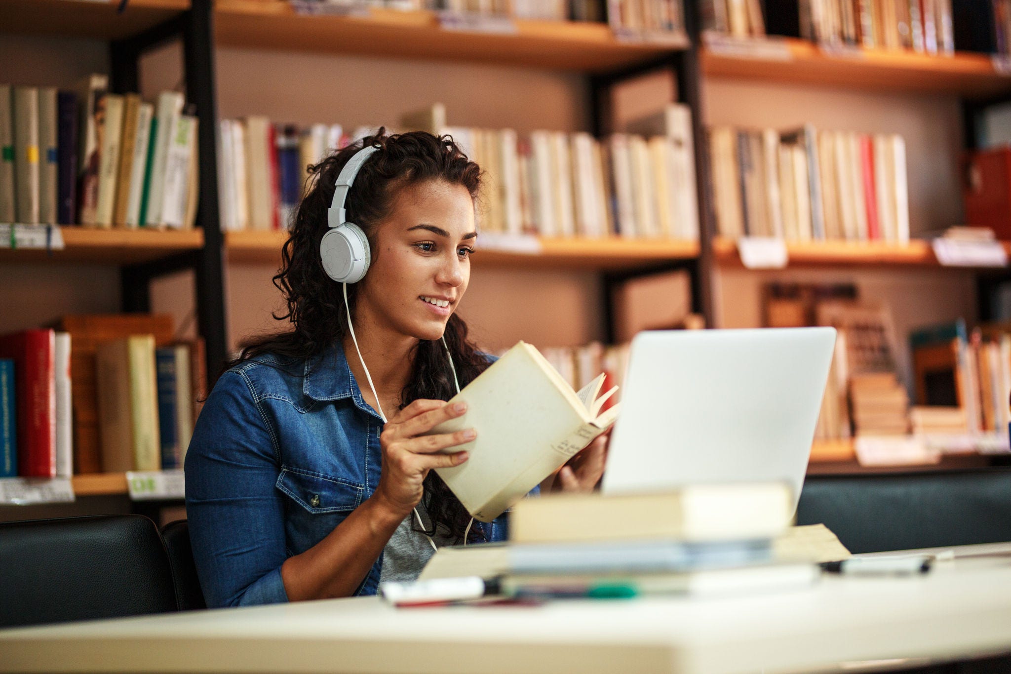 Studentin mit Kopfhörern vor Laptop in Bibliothek