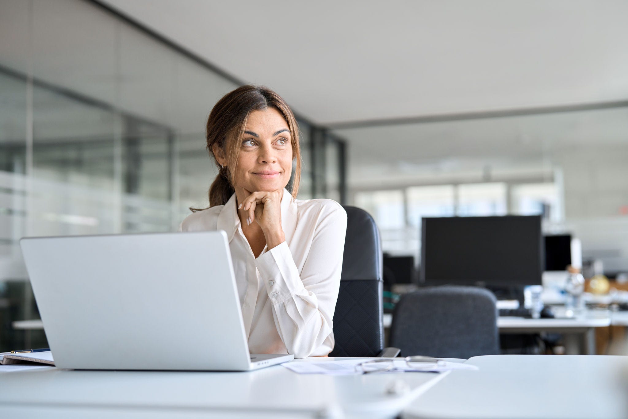 Frau mit hoffnungsvollem Blick sitzt vor Laptop in Büro.